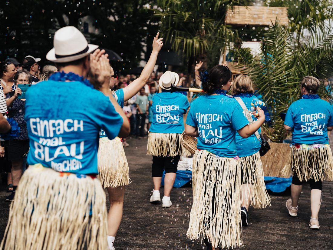 Tanzgruppe in blauen Hemden und Baströcken beim Festumzug